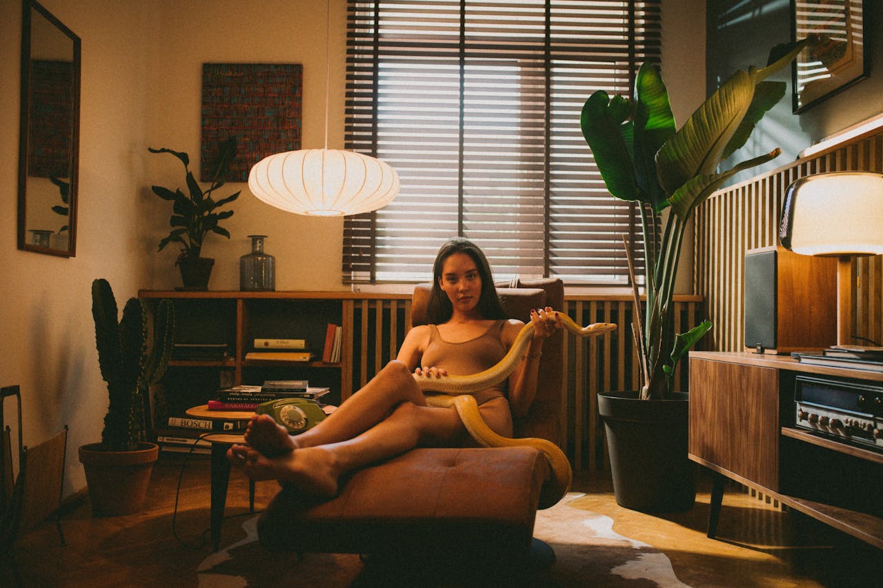 A woman sits in a warm, inviting living room, barefoot and holding a snake.